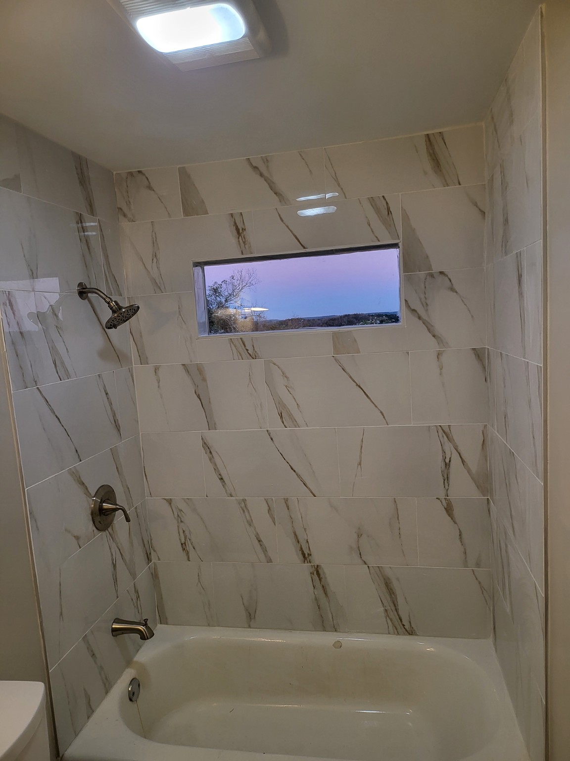 Finished tub area with marble-look tile and a horizontal window