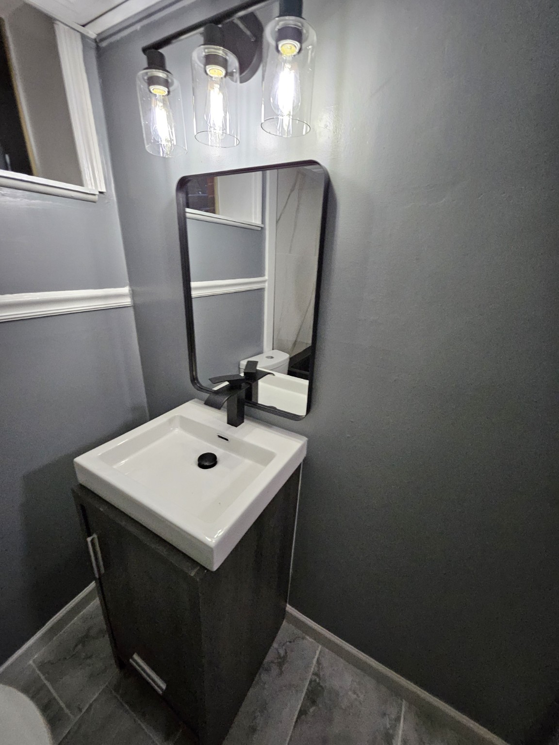 Finished vanity with black faucet, mirror, and three-light fixture