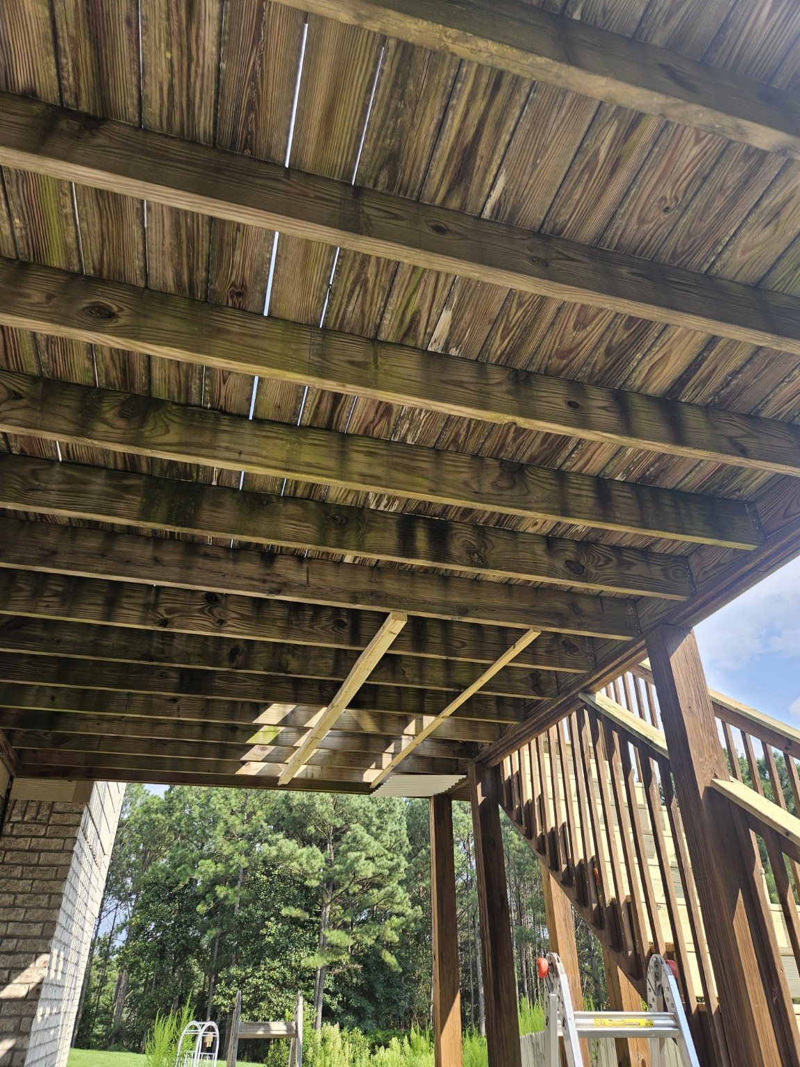 Exposed wood framing and boards beneath the deck before waterproofing and painting