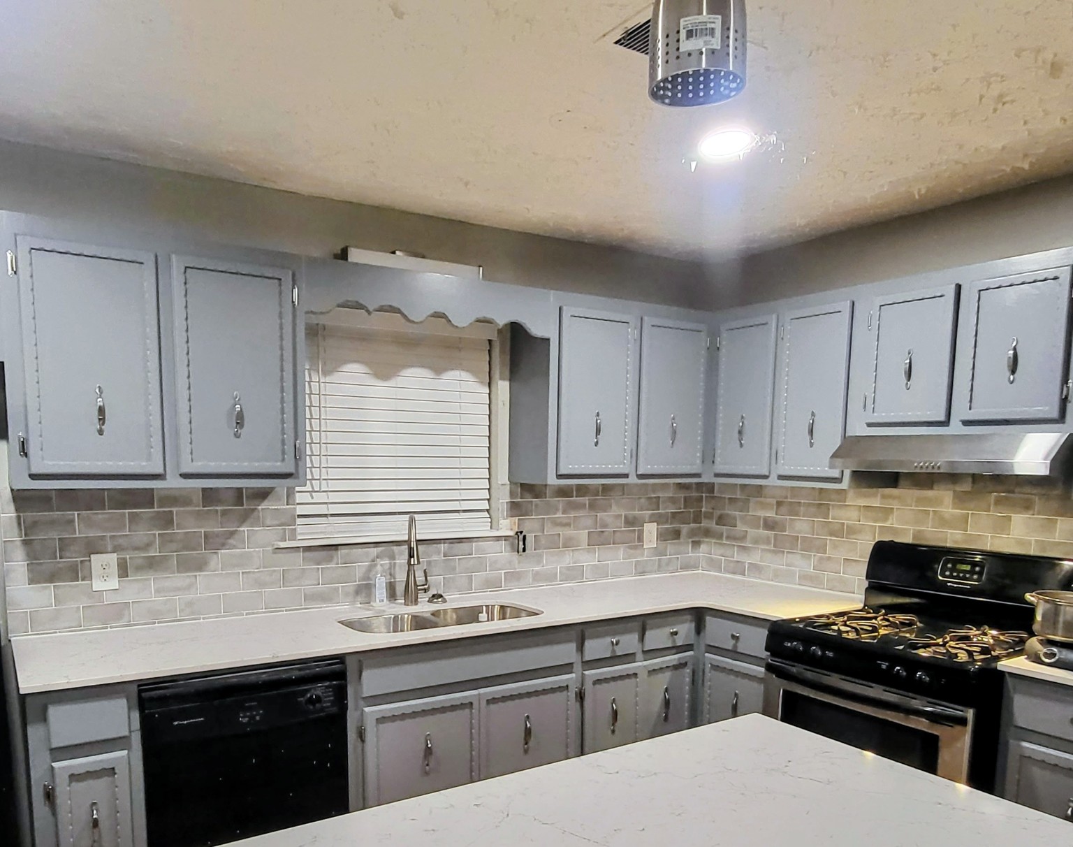 Finished gray kitchen with white counters, tile backsplash, and stainless range hood