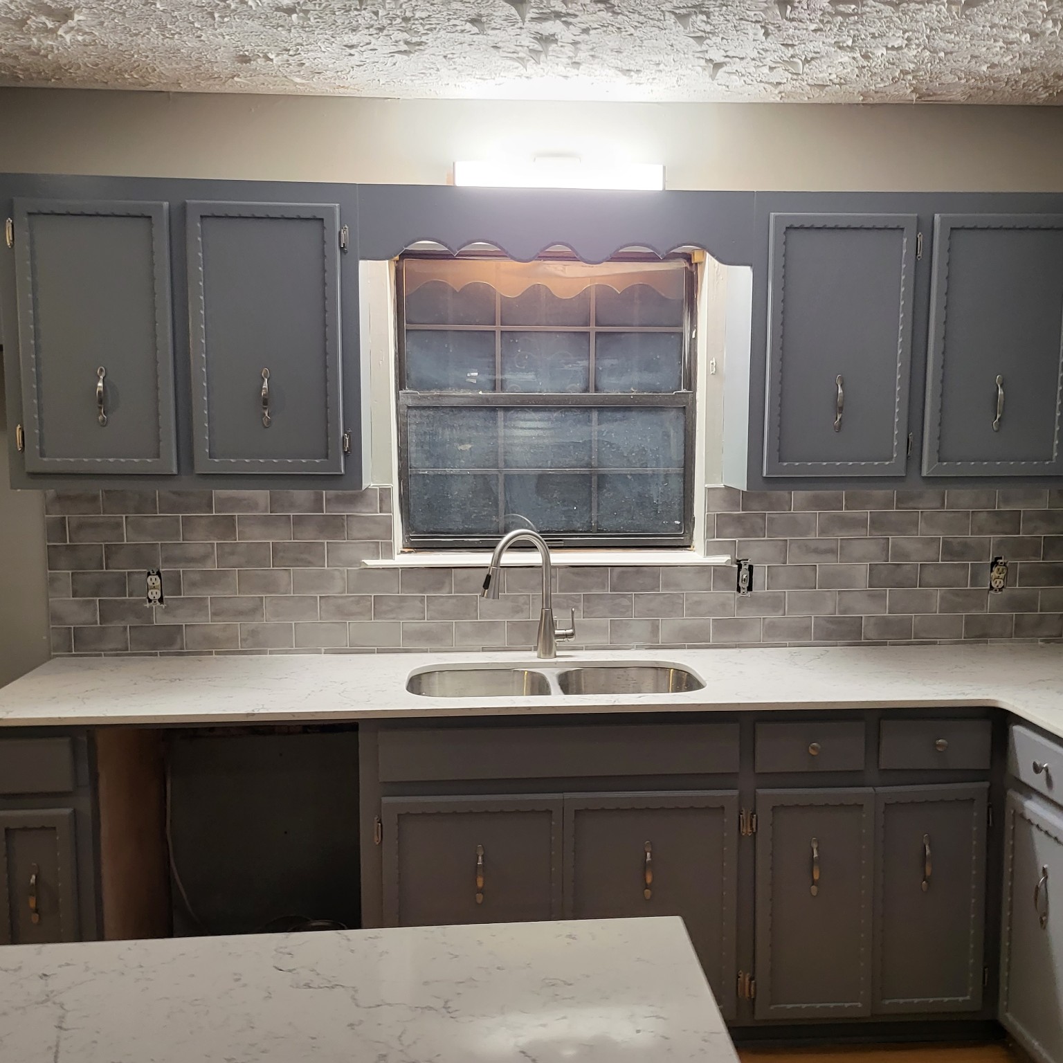 Gray kitchen cabinets with counters and backsplash installed while fixtures remain unfinished