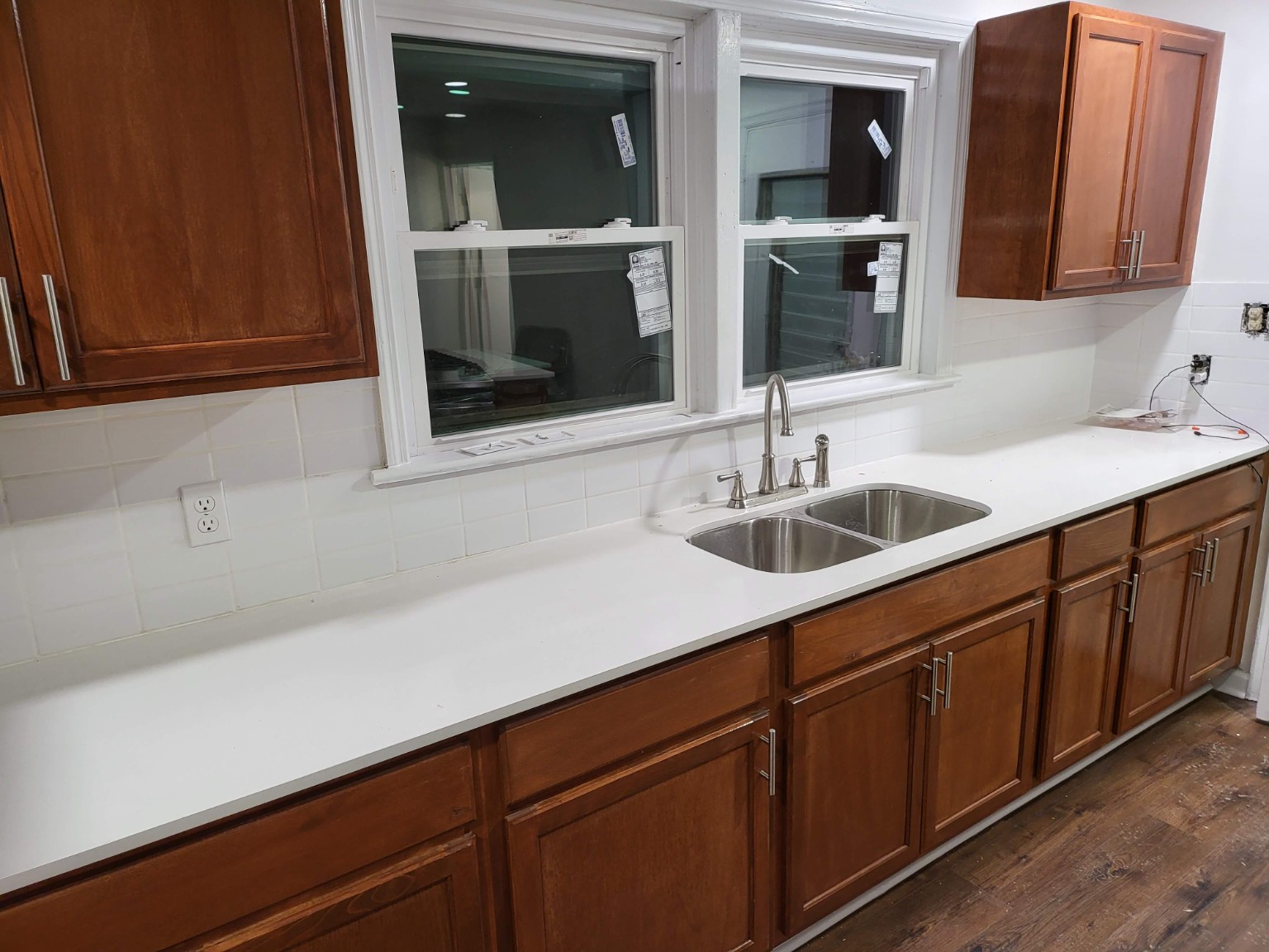 Double sink beneath new windows with white countertop and wood cabinets